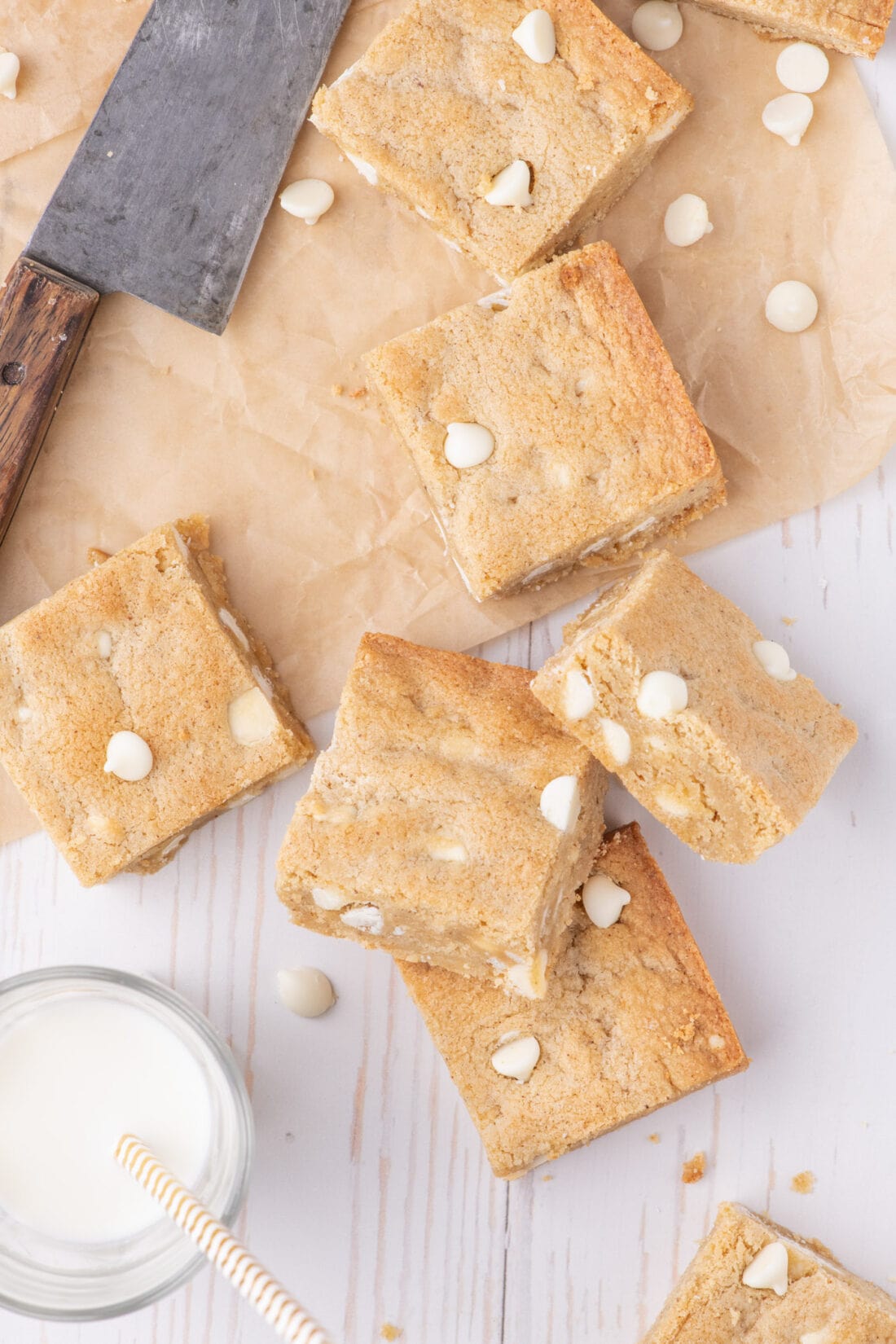 Blondies resting on parchment paper with a glass of milk