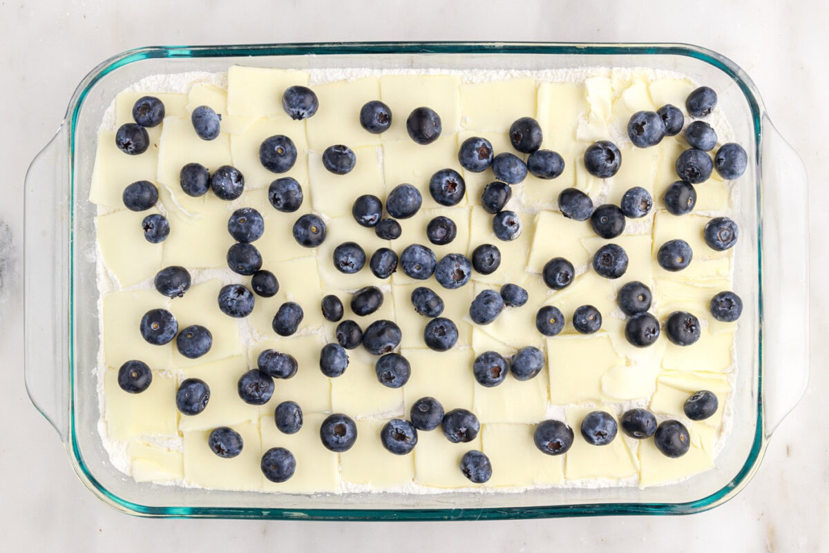 blueberry speckled on top of butter and cake mix in a baking dish