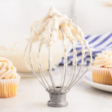 Brown Butter Frosting on a whisk attachment for mixer with cupcakes behind it