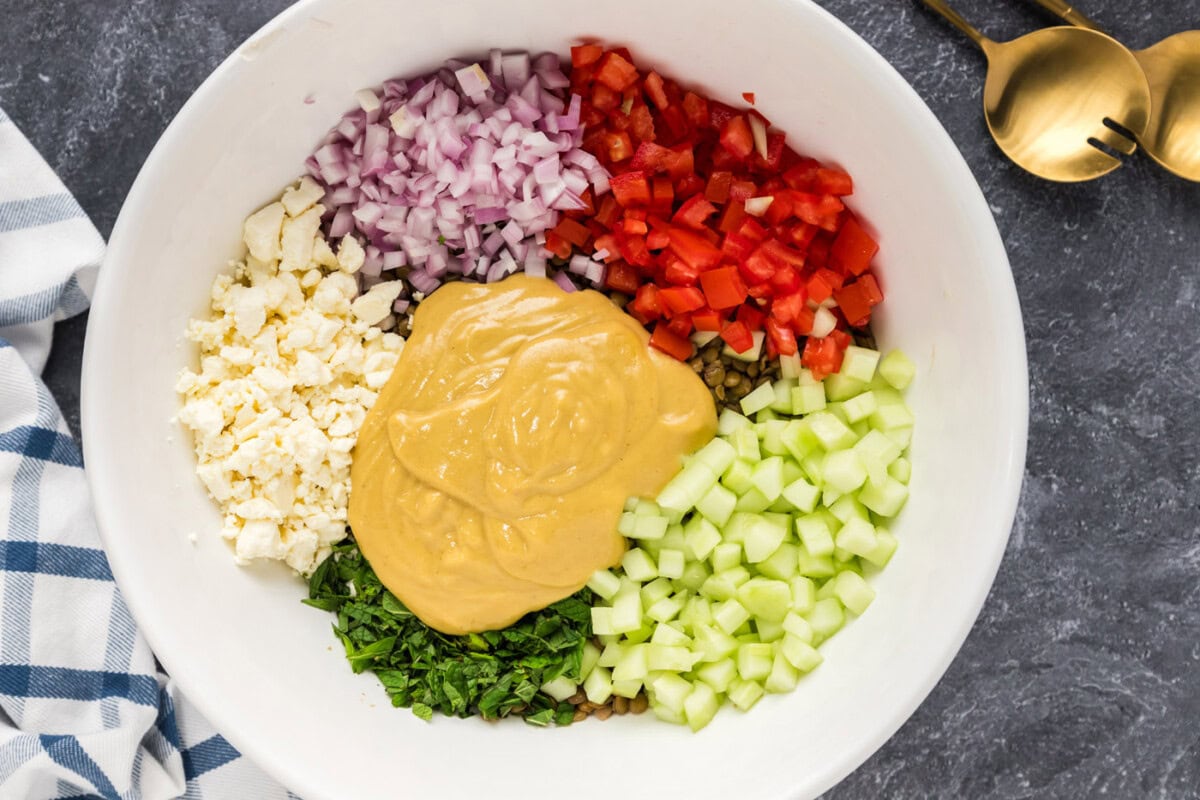 adding dressing to lentil salad ingredients in a mixing bowl
