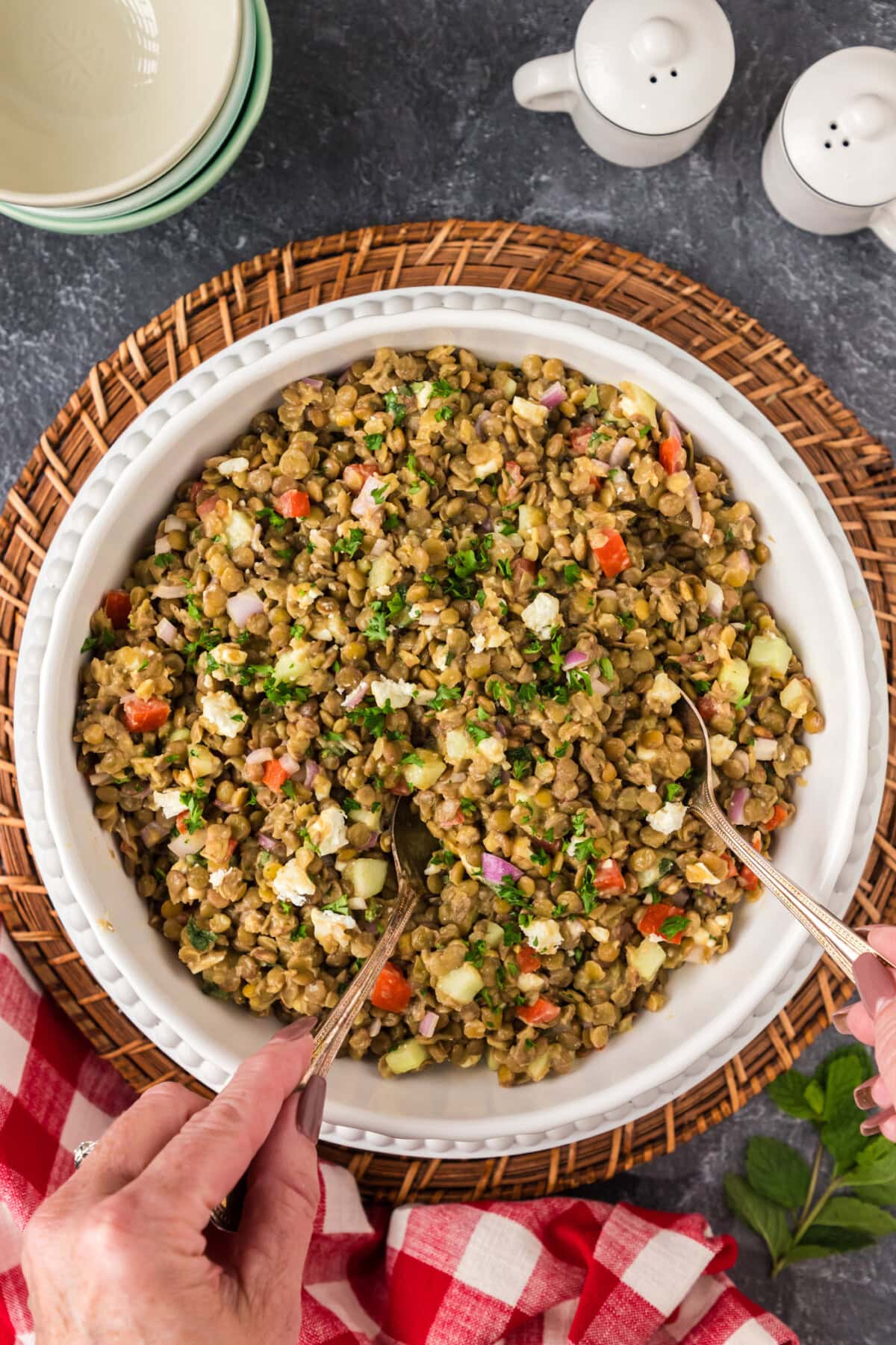 Hands holding spoons in a bowl of Lentil Salad