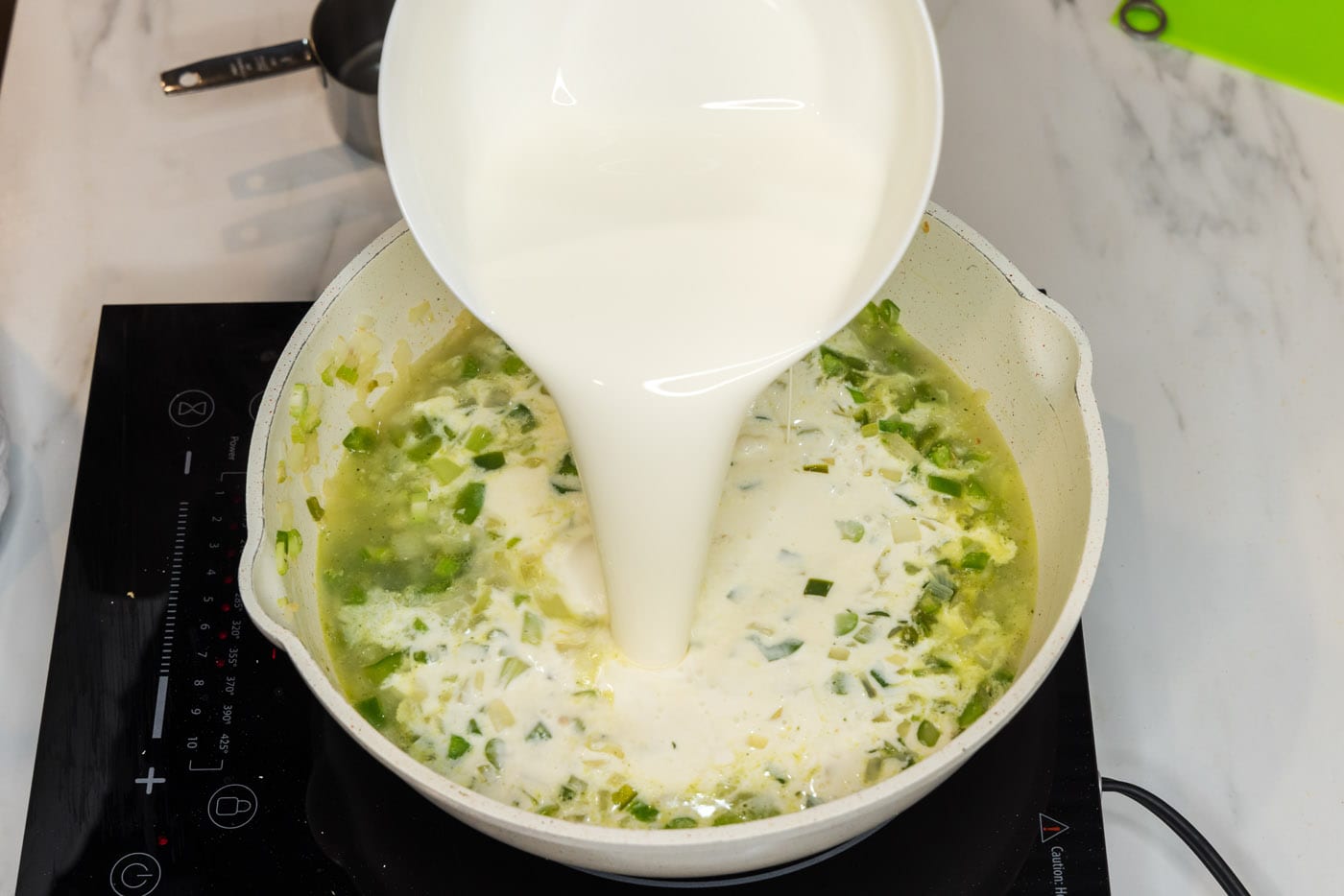 pouring heavy cream into skillet with chopped sauteed vegetables