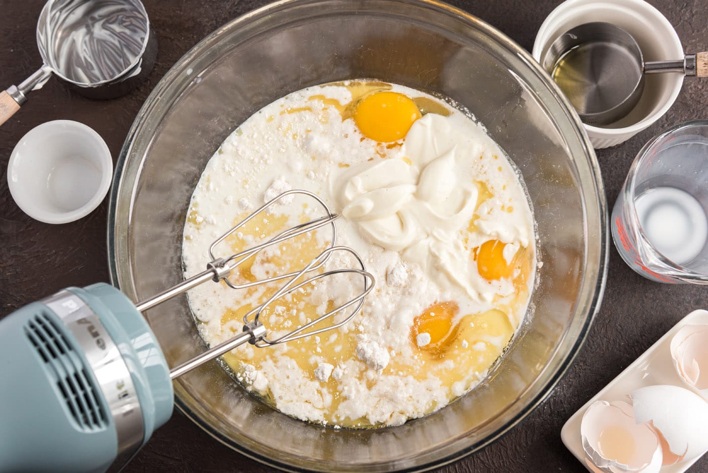cake mix ingredients with yogurt and milk in a bowl with a mixer