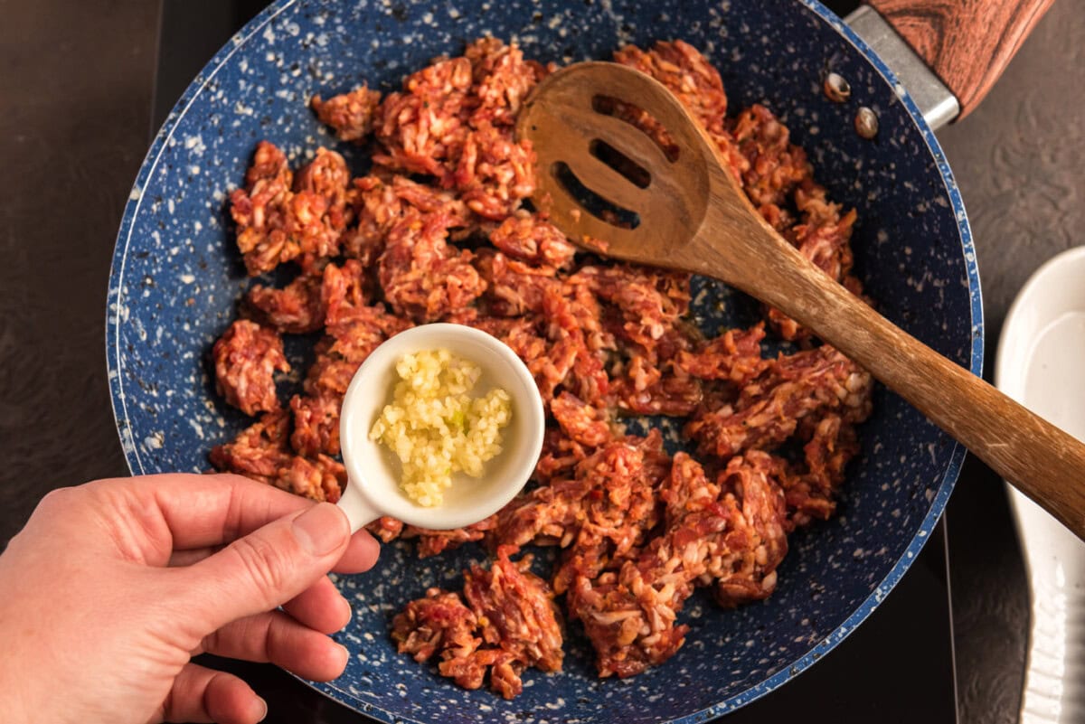 adding garlic to pan with ground pork sausage