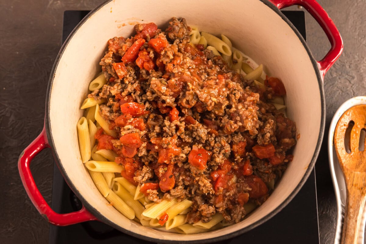 adding tomato and sausage sauce to pan with pasta