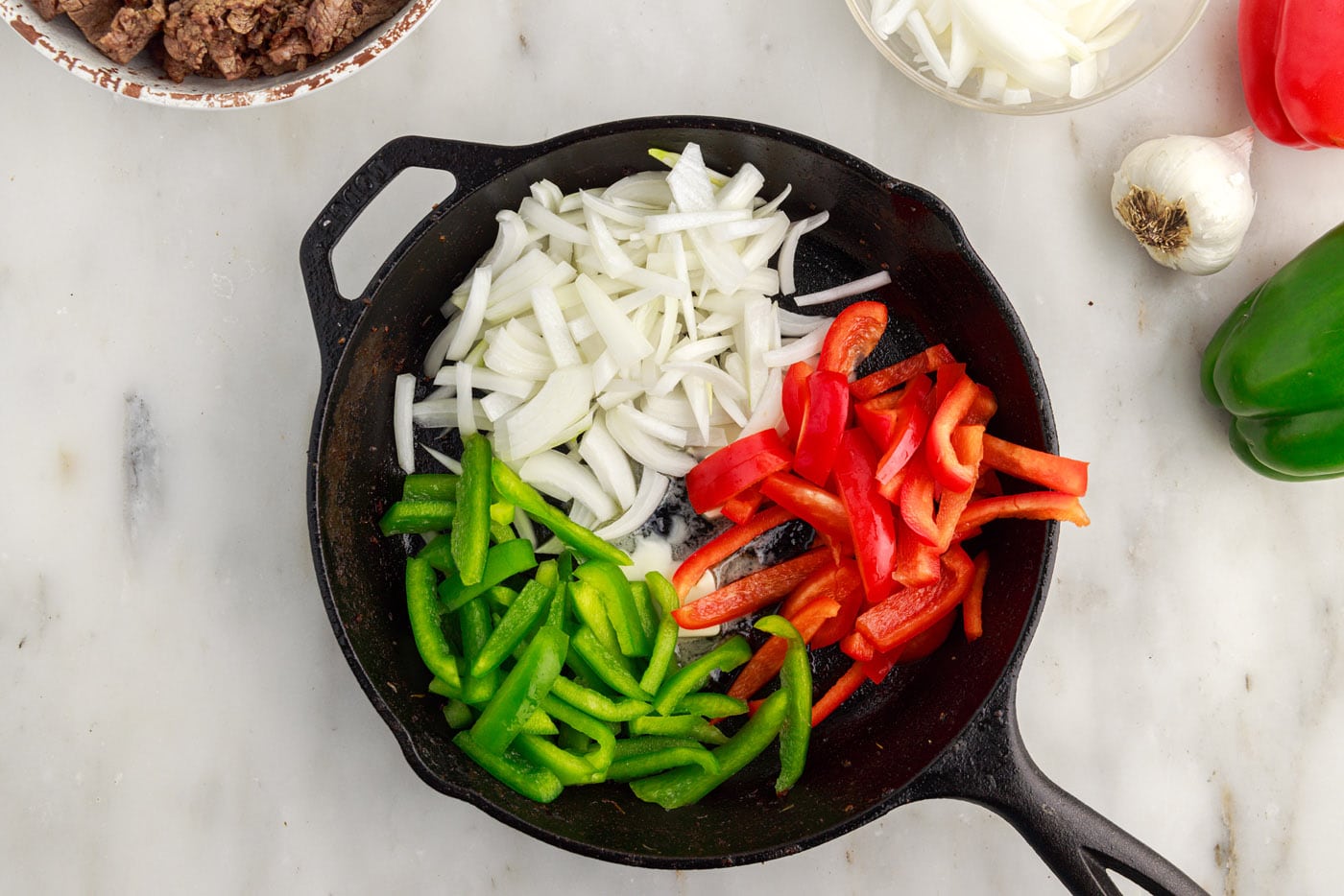 sliced bell peppers and onions in a cast iron skillet