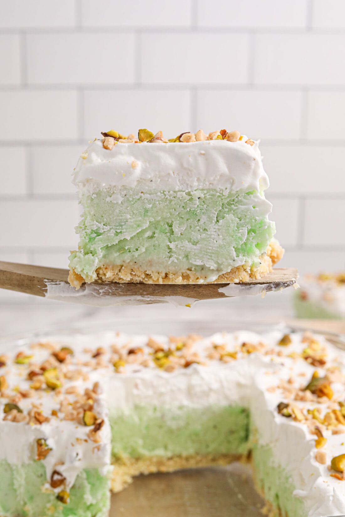 Slice of Pistachio Ice Cream Cake on a spatula being lifted above the pan