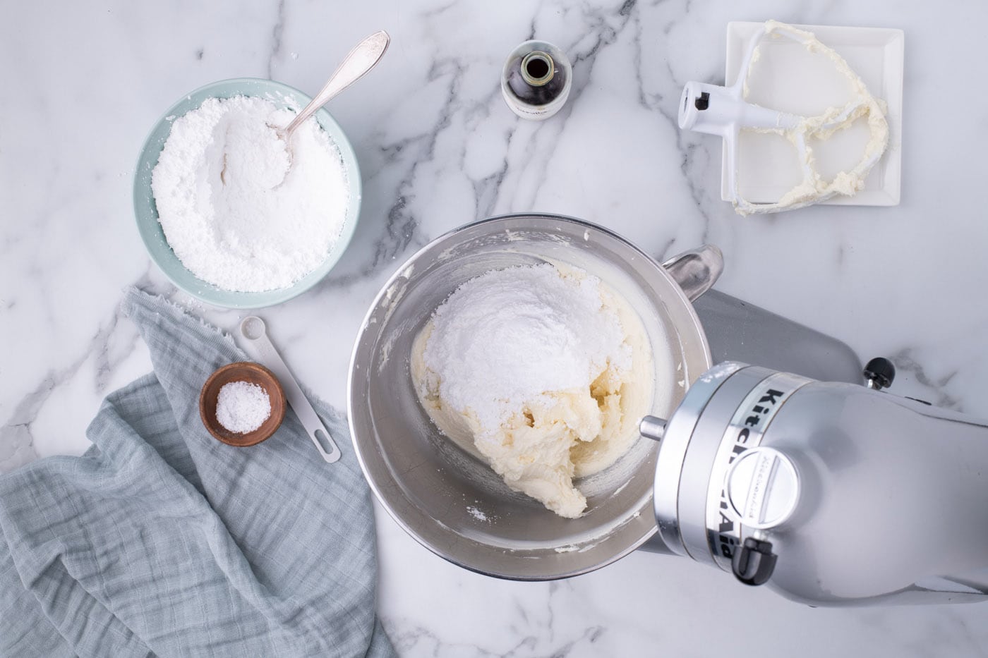 adding powdered sugar to cream cheese frosting in a mixer bowl