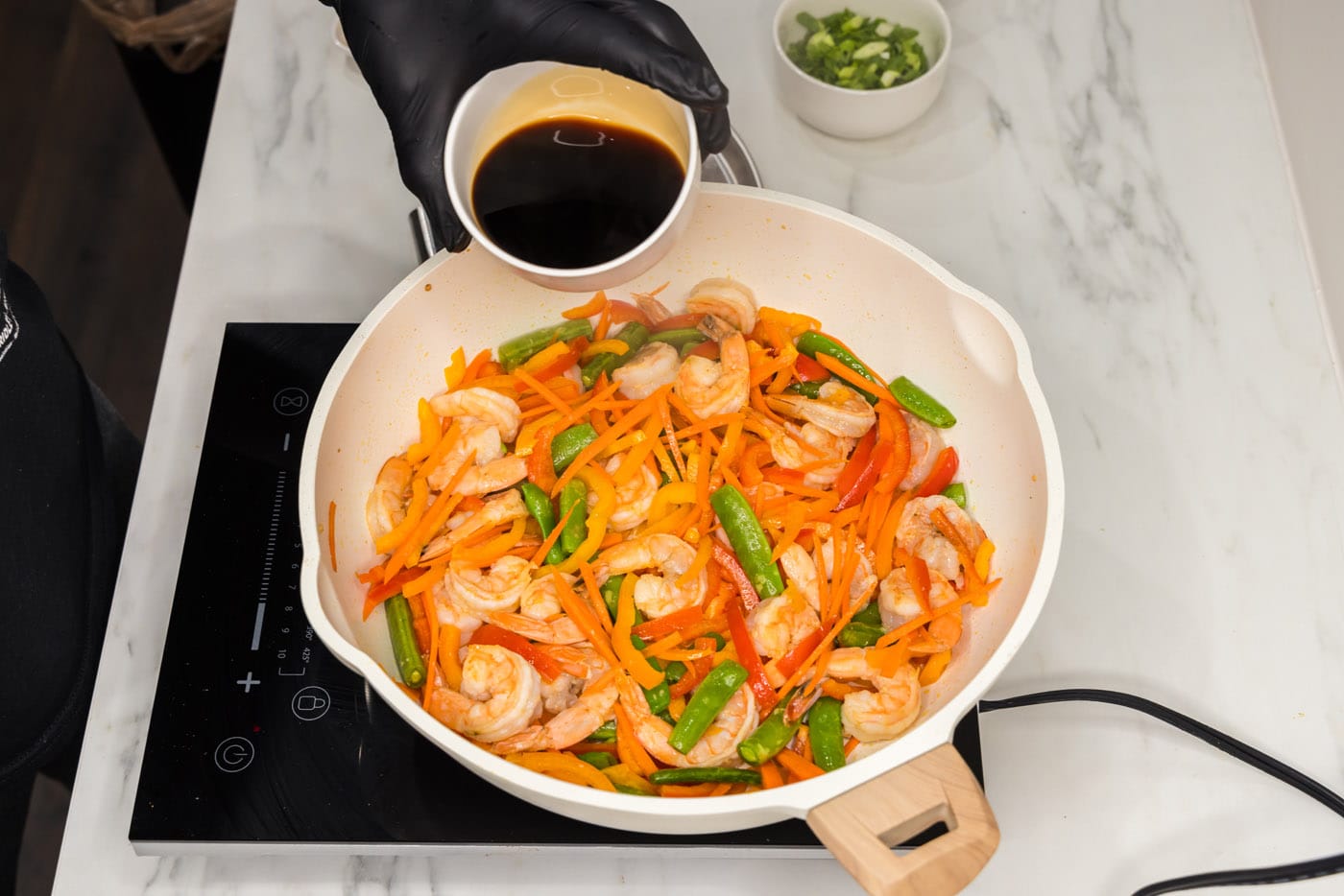 pouring soy sauce into skillet with shrimp stir fry