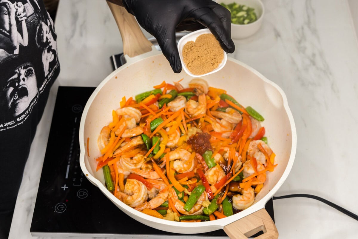 adding brown sugar to shrimp stir fry in a skillet