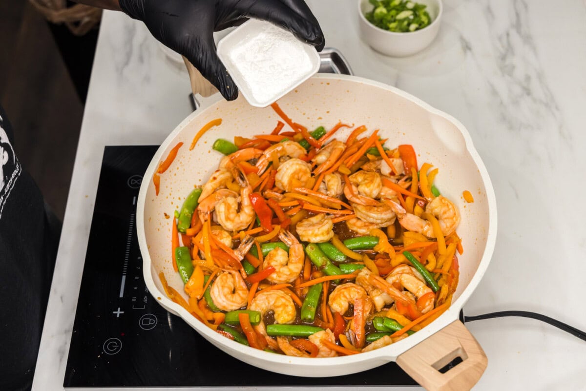 adding cornstarch to stir fry shrimp in a skillet
