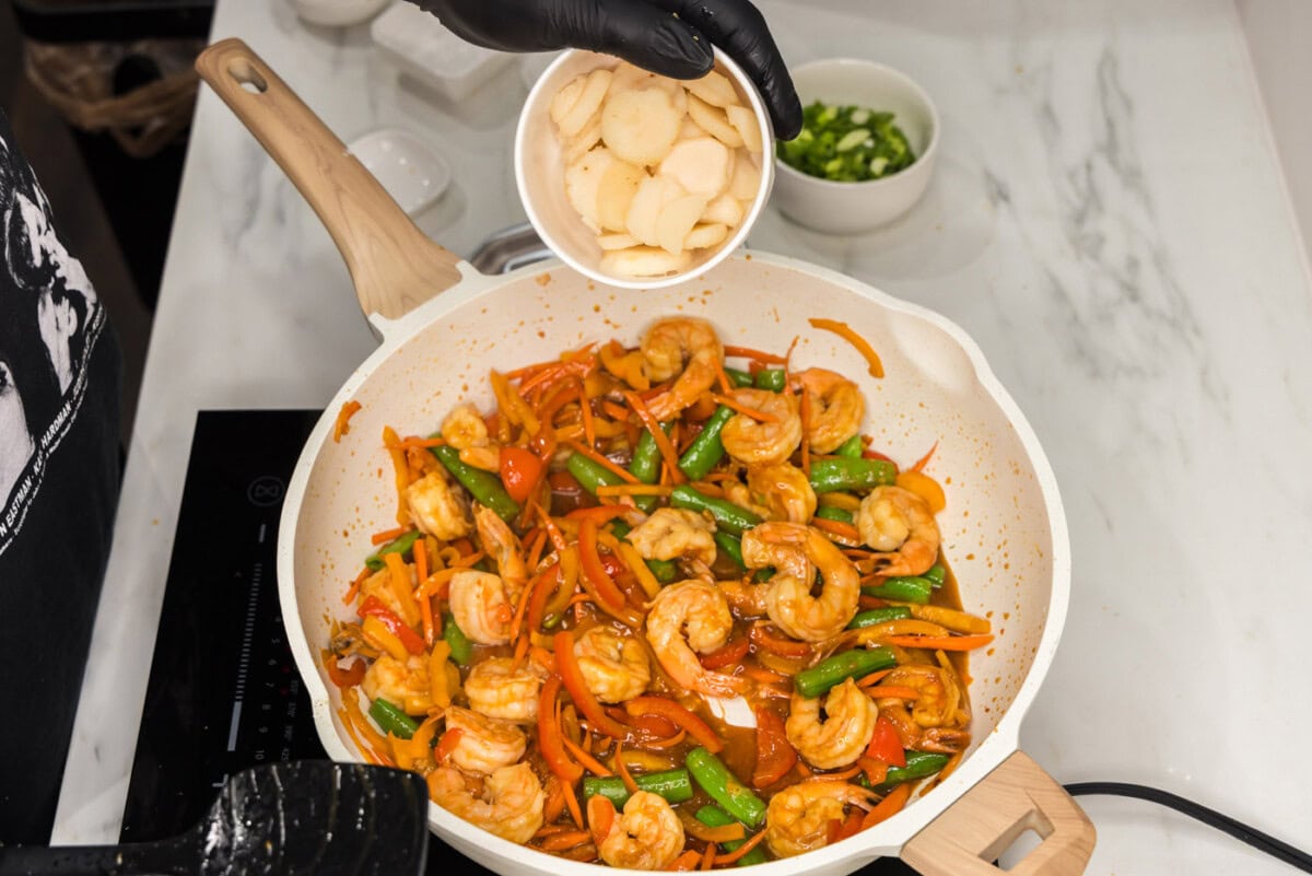 adding water chestnuts to skillet with shrimp and veggies