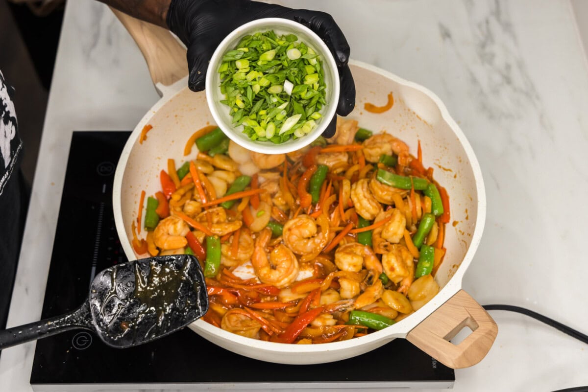 green onions over top skillet of shrimp and stir fry vegetables