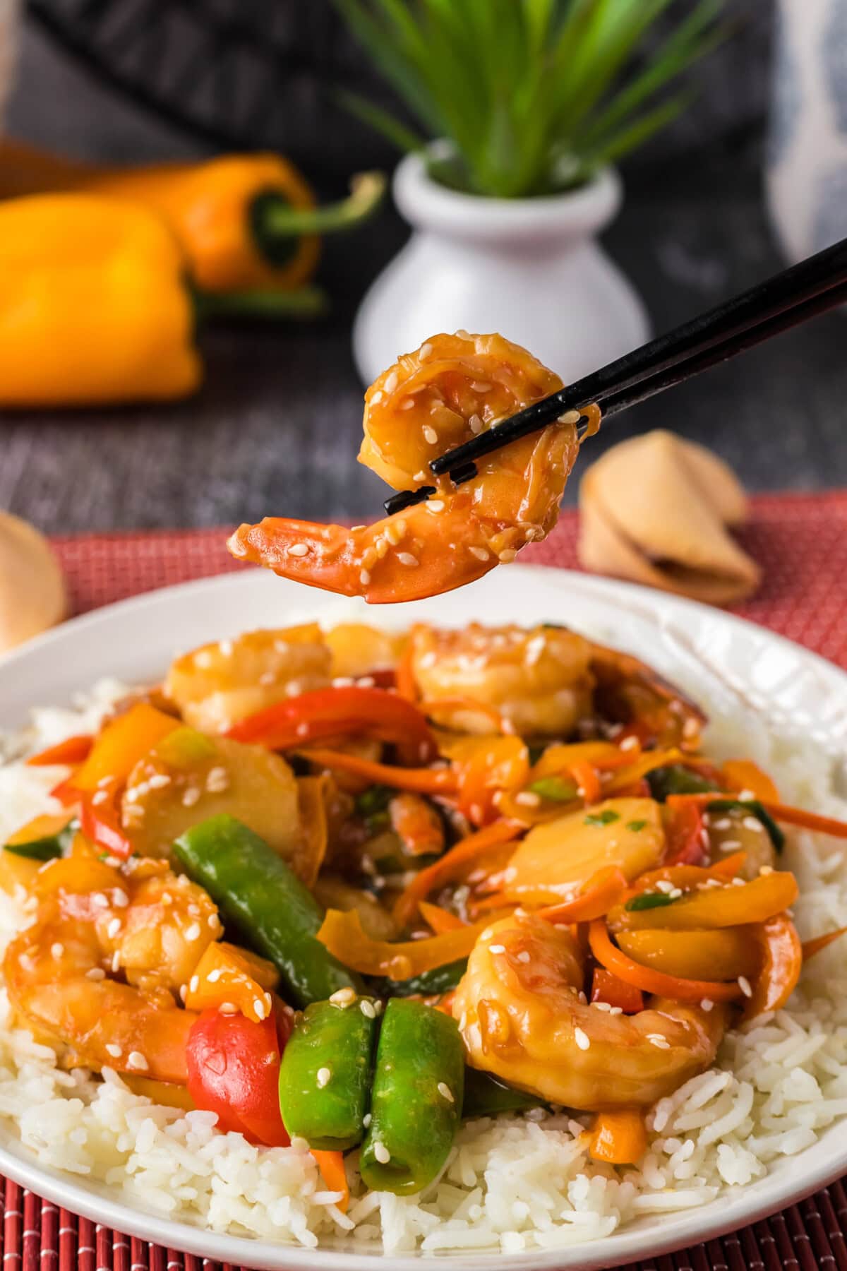 Chopsticks holding up a piece of shrimp over a plate of Shrimp Stir Fry