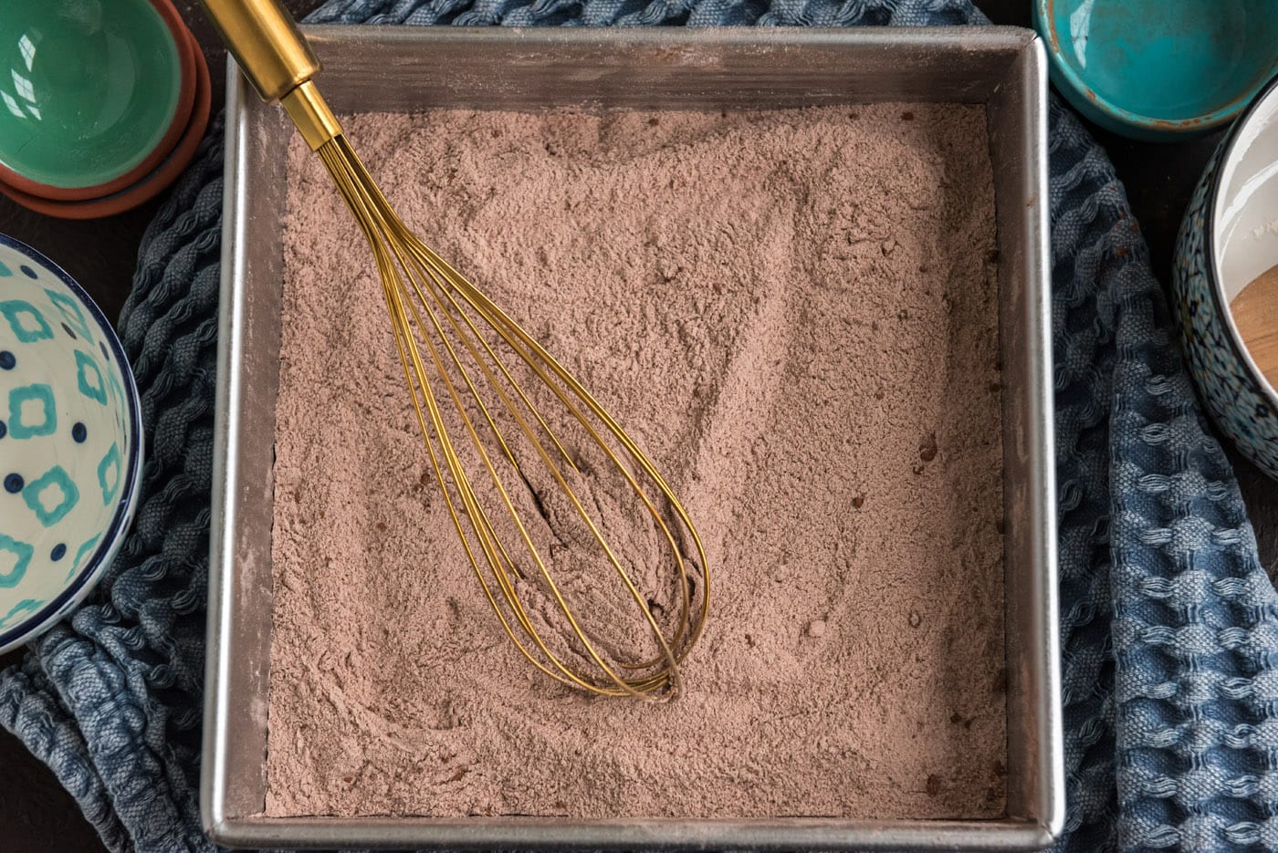 dry cake ingredients in a metal baking pan with a whisk