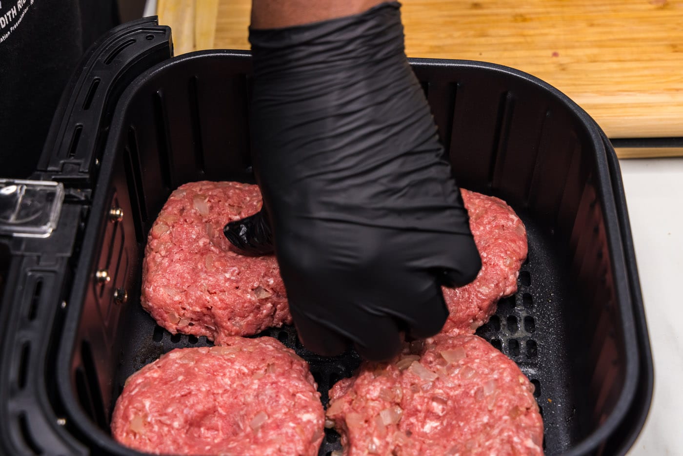 thumb pressing an indent into burger patties in the air fryer