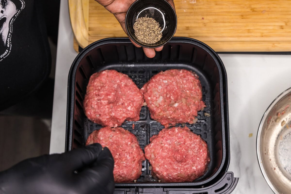 sprinkling burger patties in air fryer with pepper