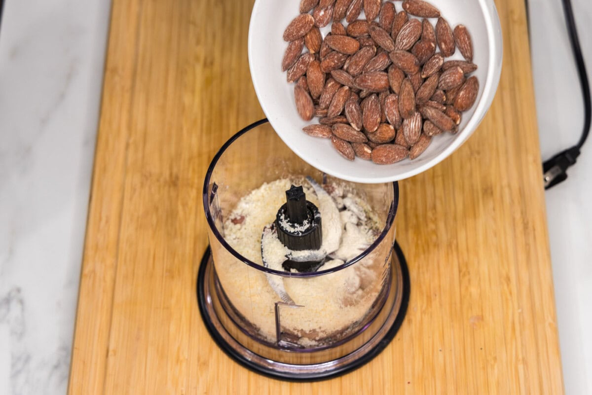 pouring almonds into food processor with seasonings and parmesan cheese