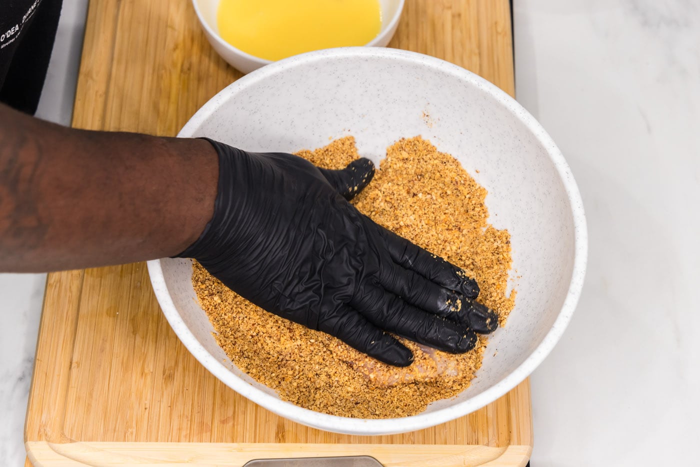 hand patting chicken breast with almond breading