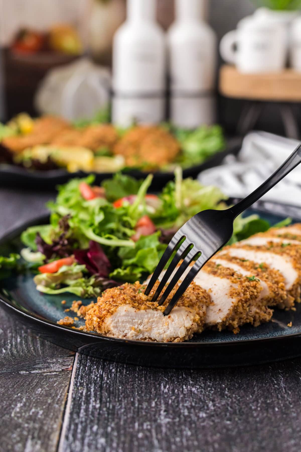 Fork in a piece of Almond Crusted Chicken with salad on the side