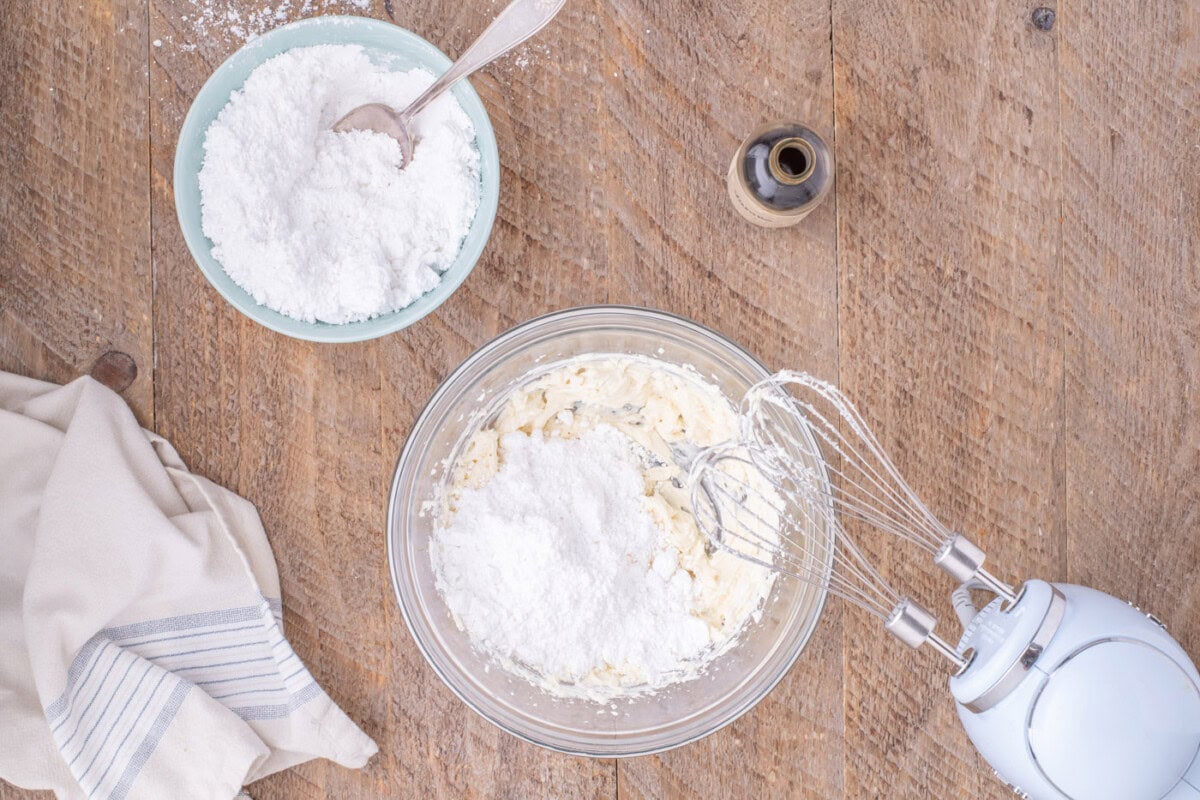 adding powdered sugar to cream cheese frosting in a bowl