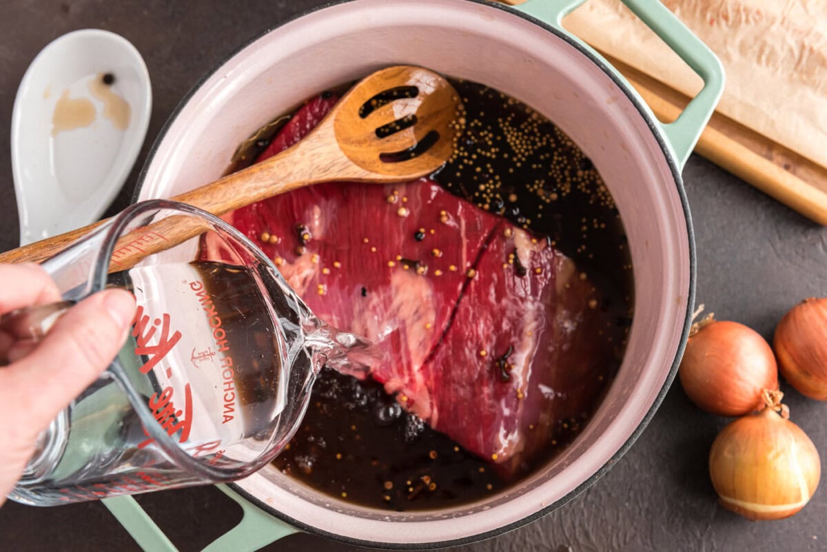 pouring water over beef brisket in a Dutch oven