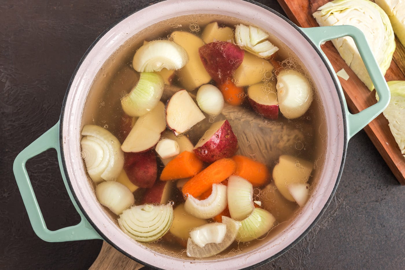corned beef in Dutch oven with potatoes, onion, and carrots