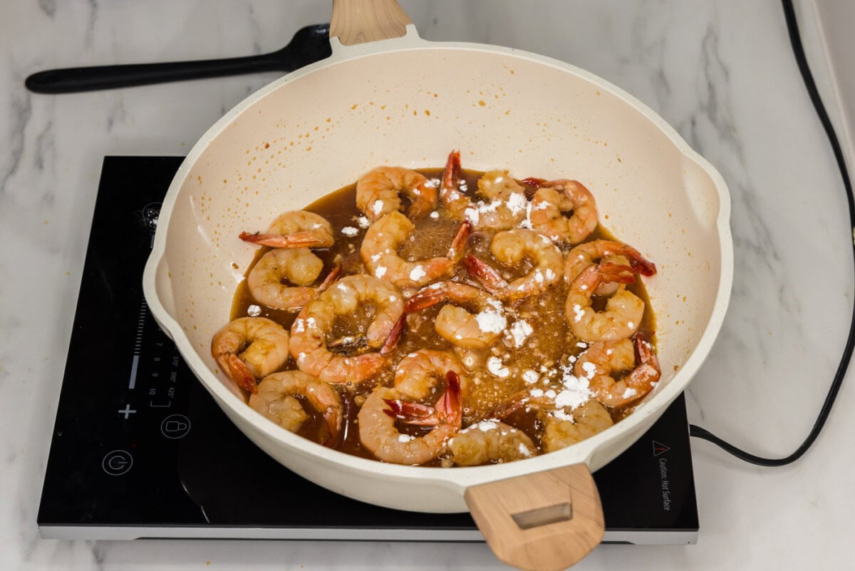 cornstarch sprinkled over honey garlic shrimp in a skillet
