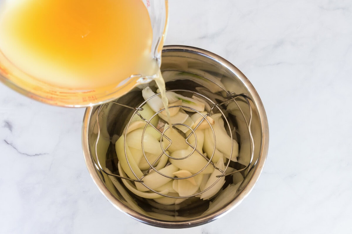 Broth being poured over onion wedges and garlic cloves