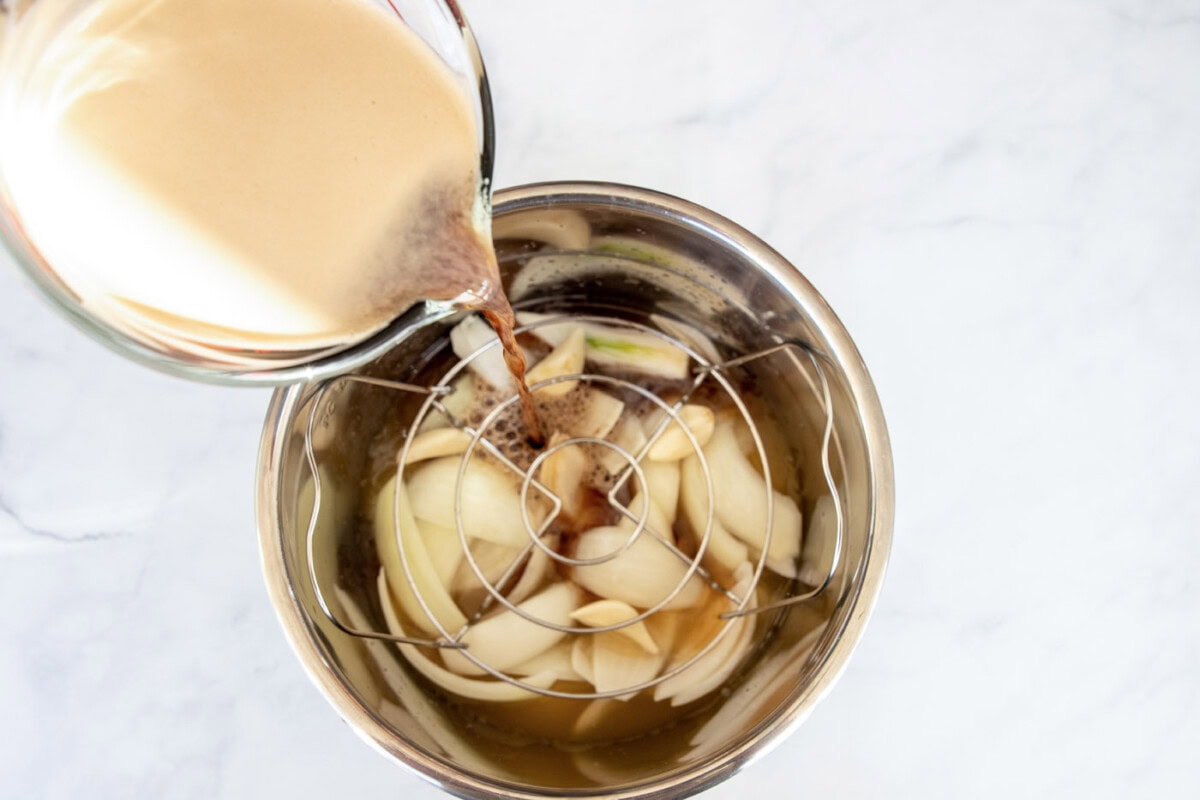 Beer being poured into an Instant Pot over onion wedges and garlic cloves
