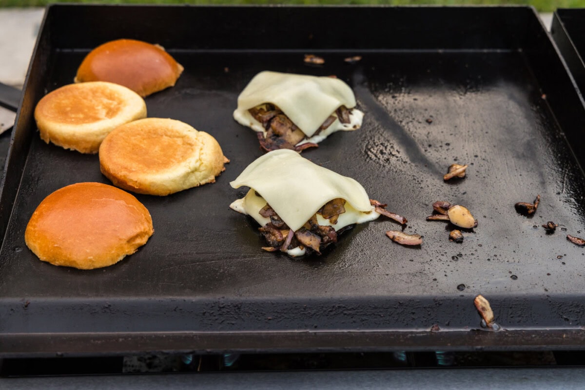 sliced mozzarella cheese on top of mushroom burgers on the grill