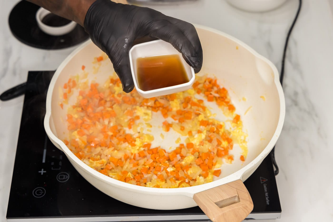 adding fish sauce to scrambled eggs and veggies in a skillet