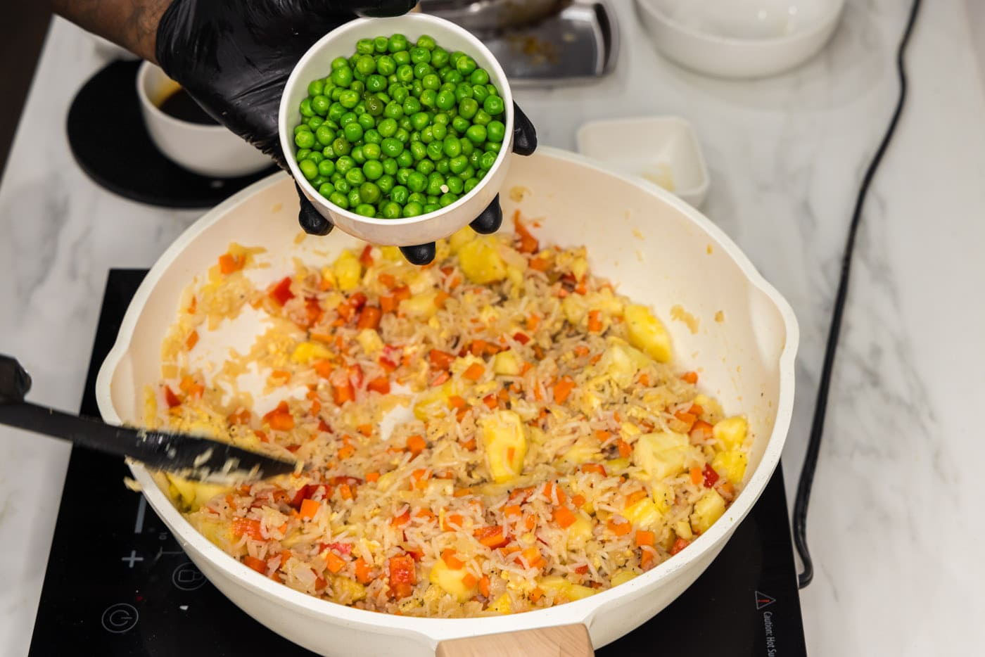 adding peas to skillet with fried rice