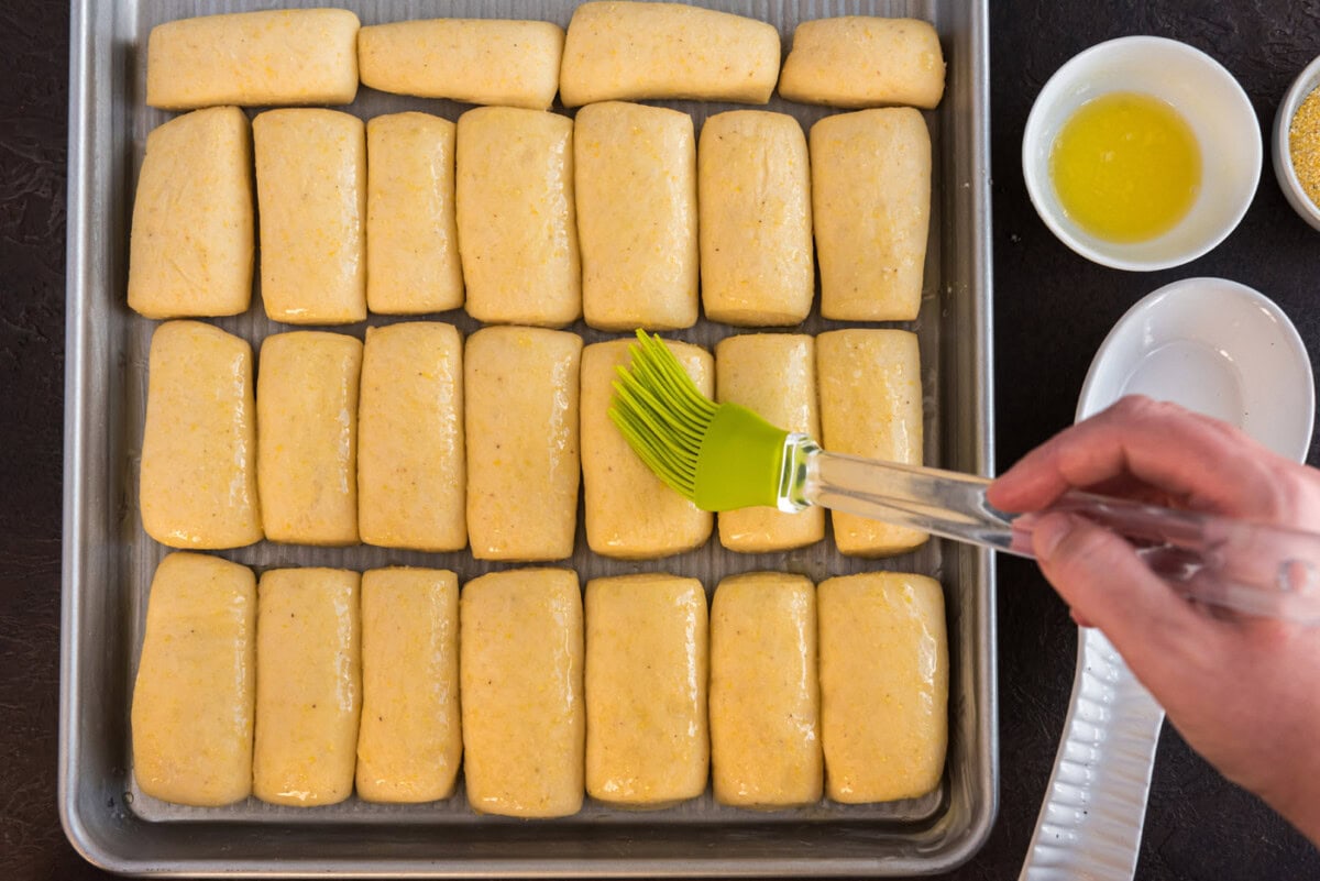brushing melted butter on top of dough on a baking sheet
