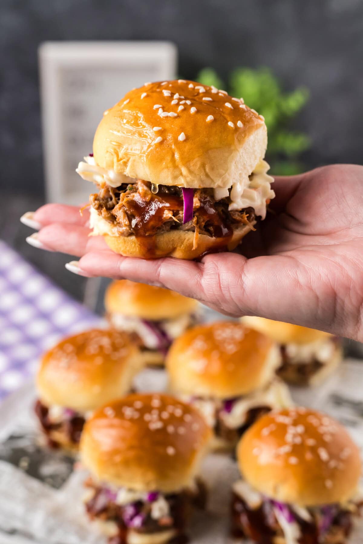 Hand holding up a Pulled Pork Slider over more Pulled Pork Sliders