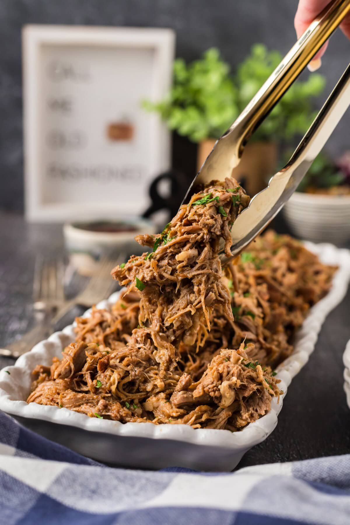 Tongs holding up pulled pork above a platter