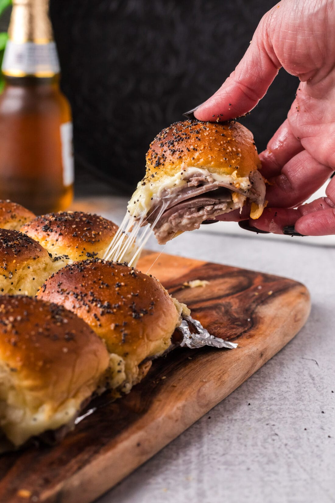 Hand pulling up a Roast Beef Slider from a board with a cheese pull