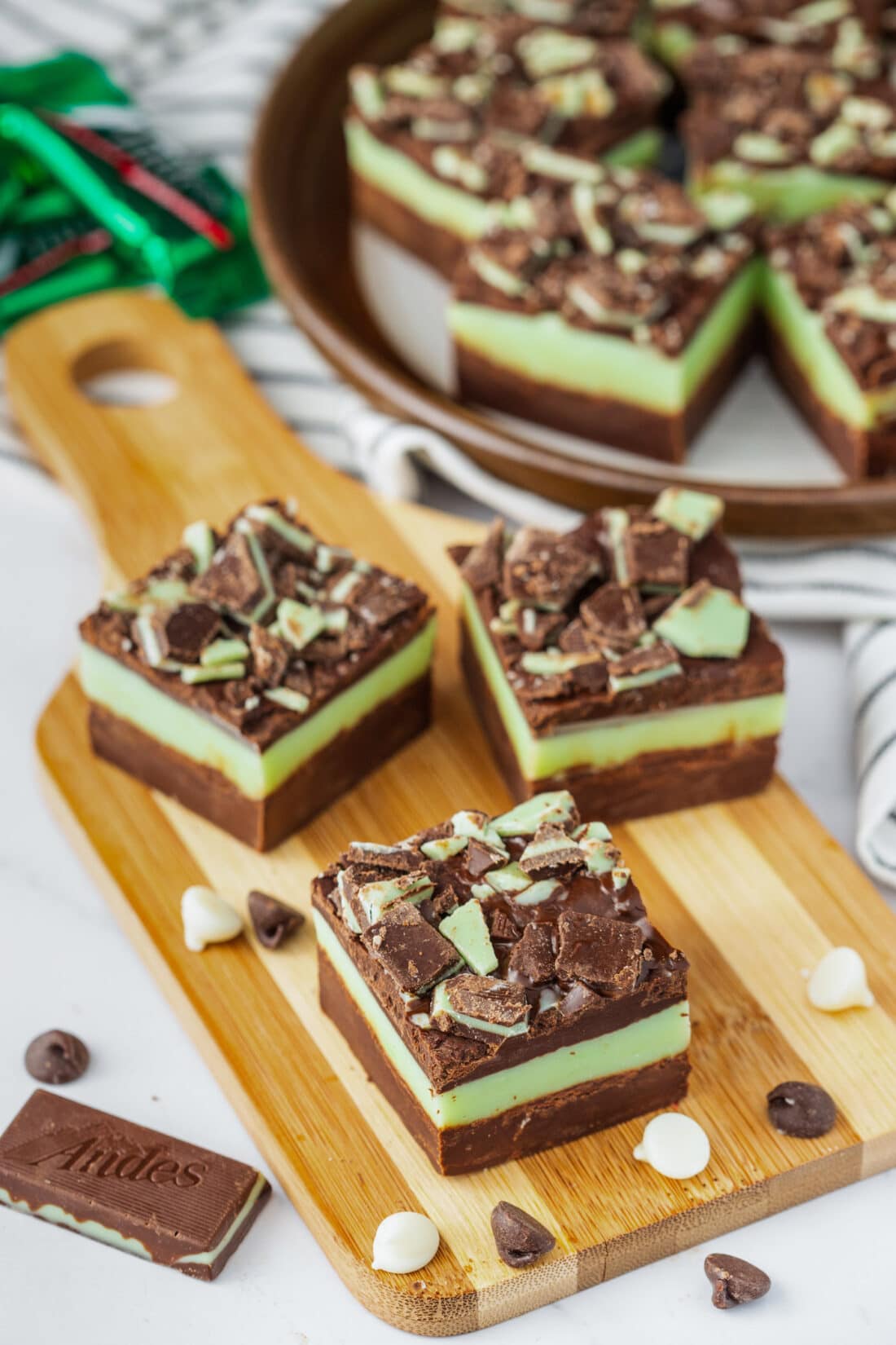Three squares of Andes Mint Fudge on a wooden board