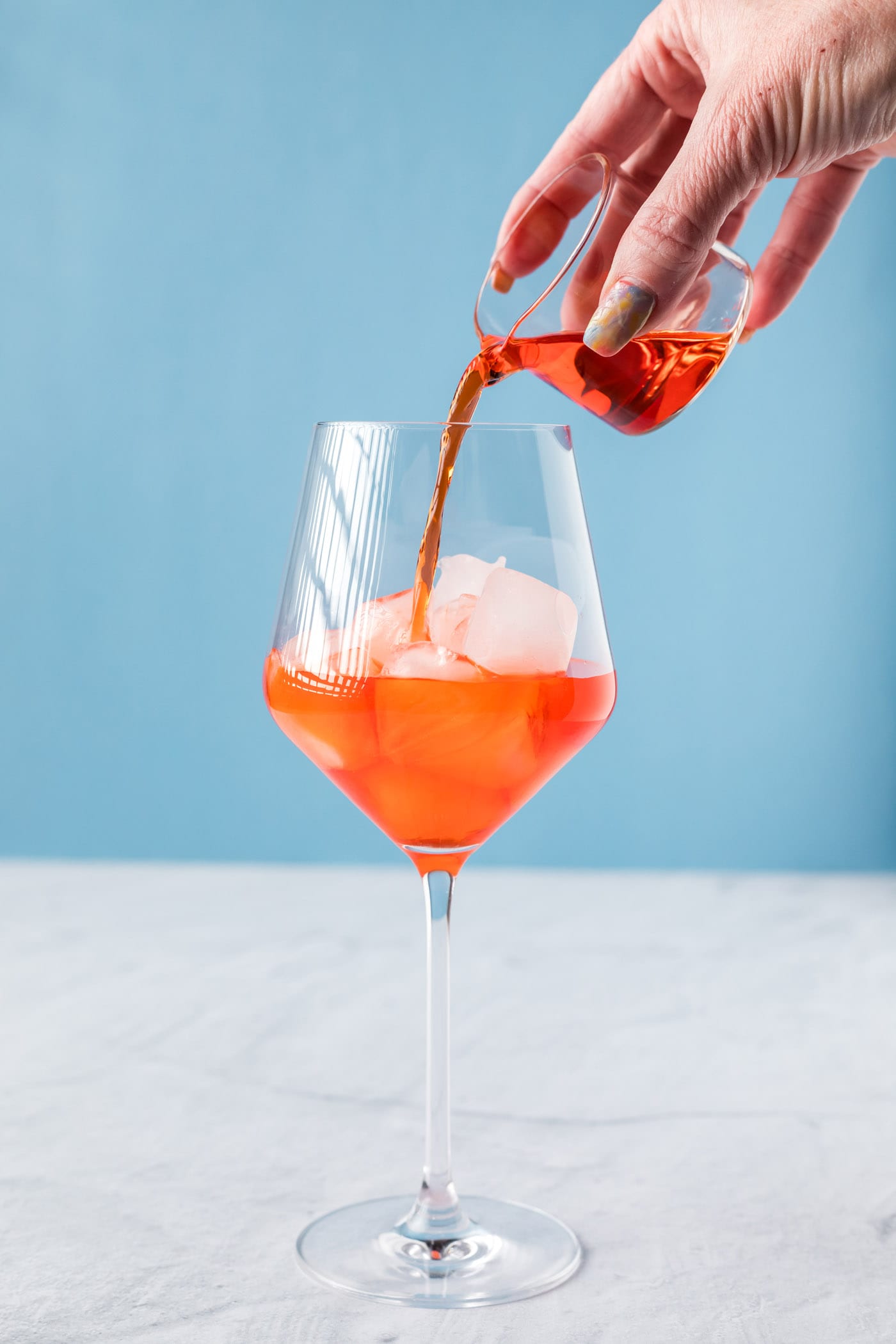 pouring Aperol into a wine glass with ice
