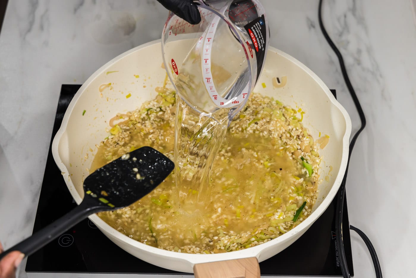 pouring water into risotto in a skillet