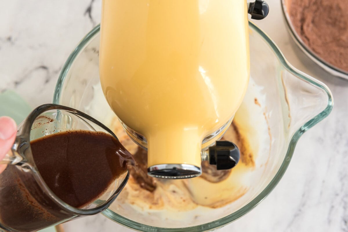 pouring melted chocolate and coffee mixture into stand mixer with cake ingredients