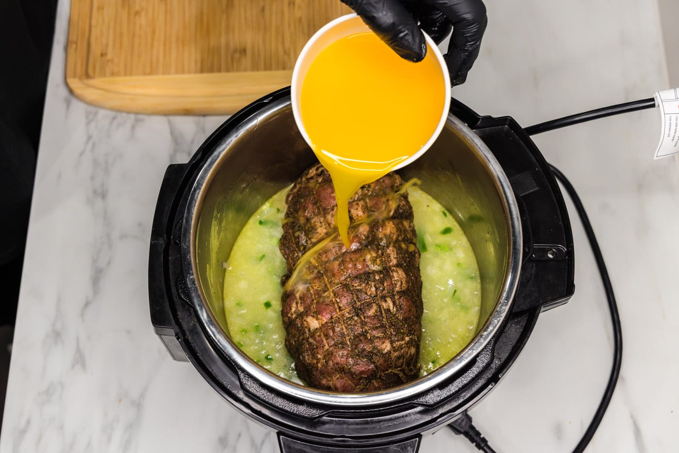 pouring orange juice into instant pot with jalapeno, onion, and pork roast