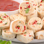 Close up photo of Mexican Pinwheels on a plate with a bowl of salsa in the background