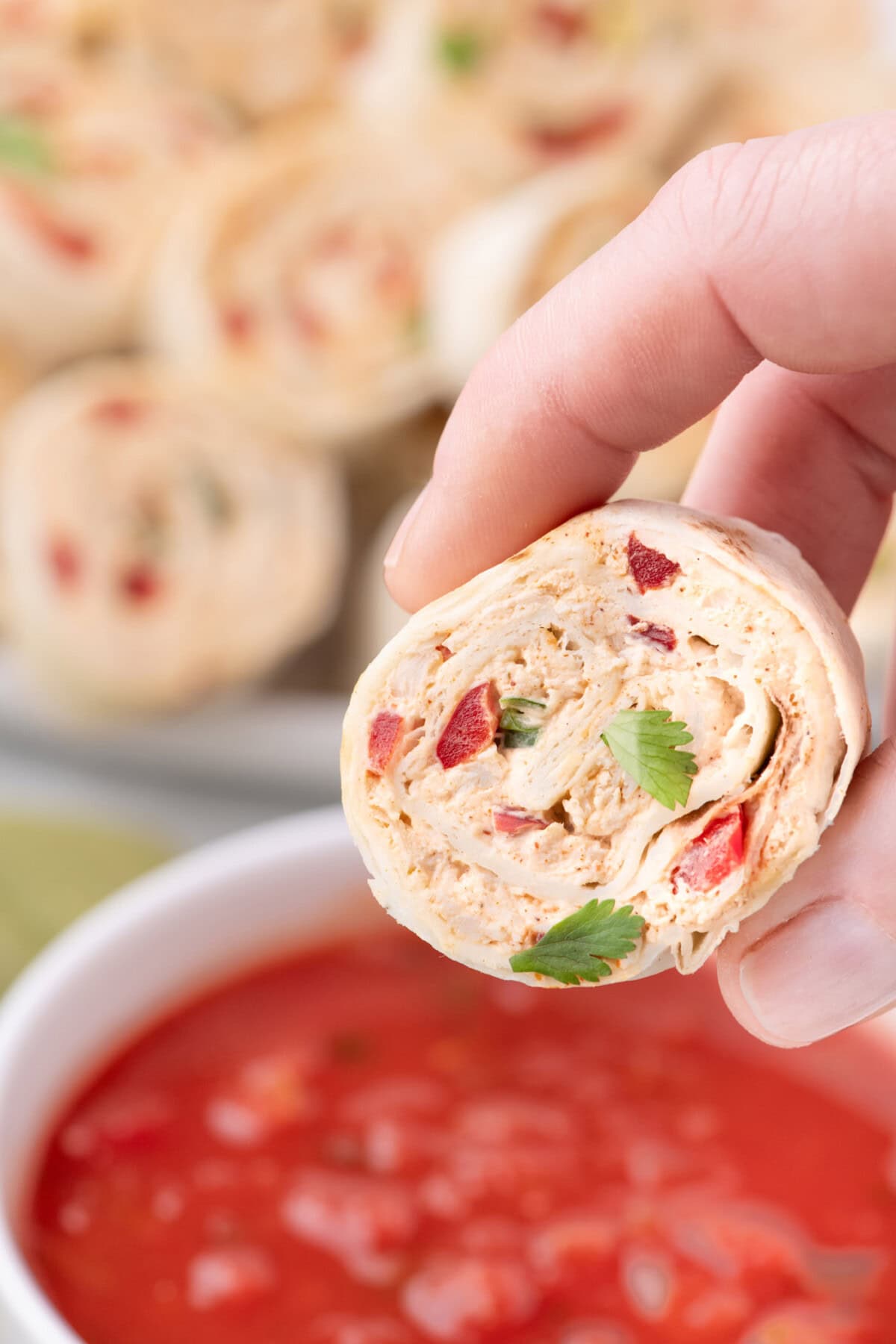 Hand holding a Mexican Pinwheel above a bowl of salsa