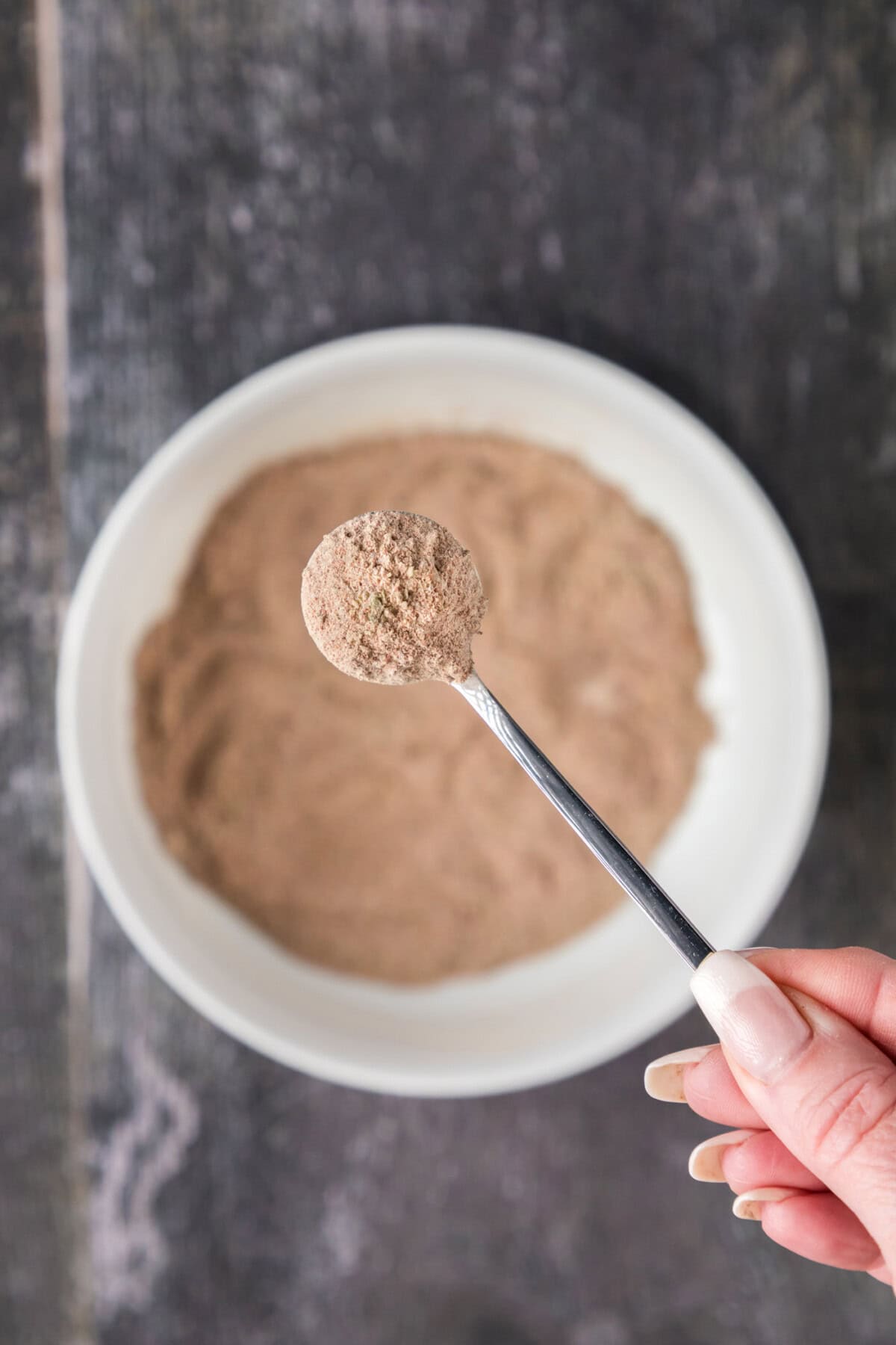 Spoonful of Mexican Seasoning held above a bowl of Mexican Seasoning