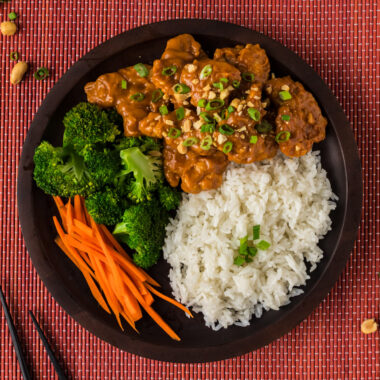 Close up photo of a plate of Peanut Butter Chicken with rice, carrots and broccoli
