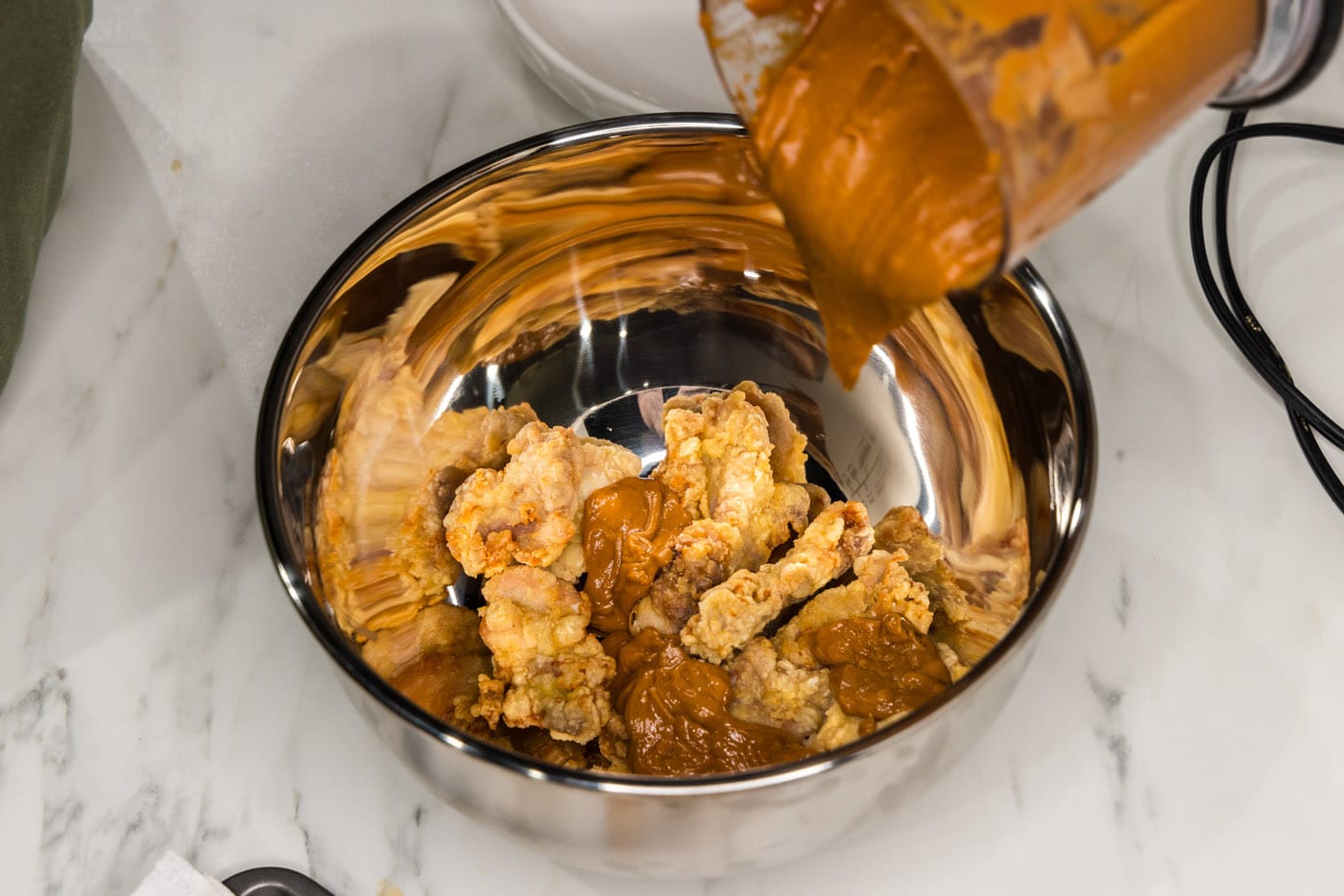 pouring peanut butter sauce over fried chicken