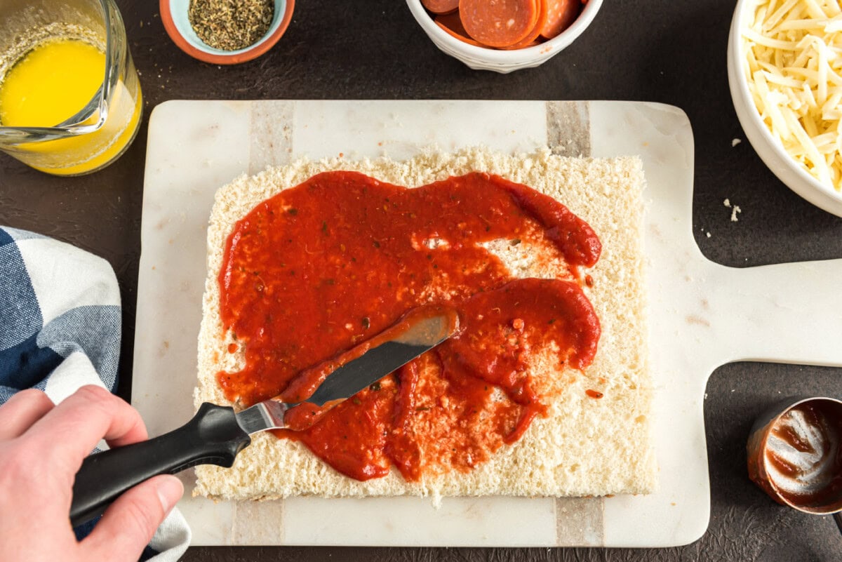 spreading pizza sauce over slider buns