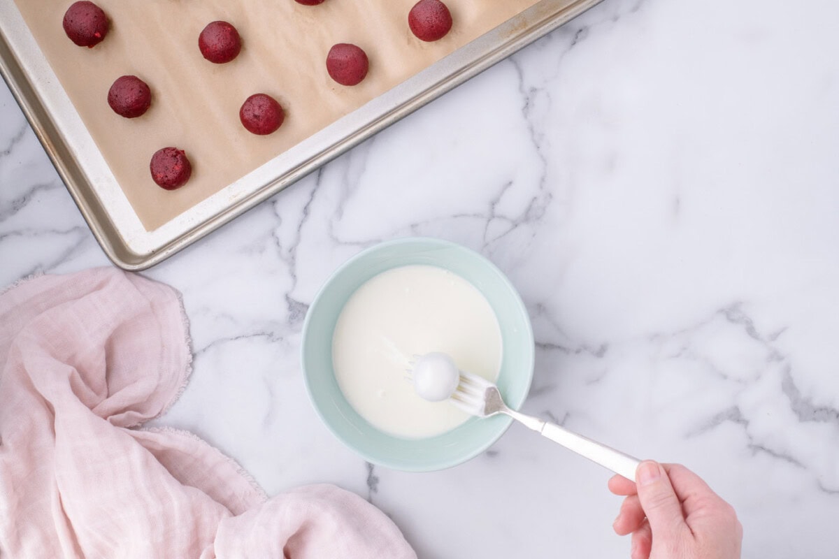 dipping red velvet cake balls in white chocolate with a fork
