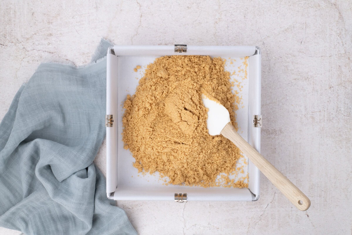 spreading graham cracker crust on bottom of a baking pa